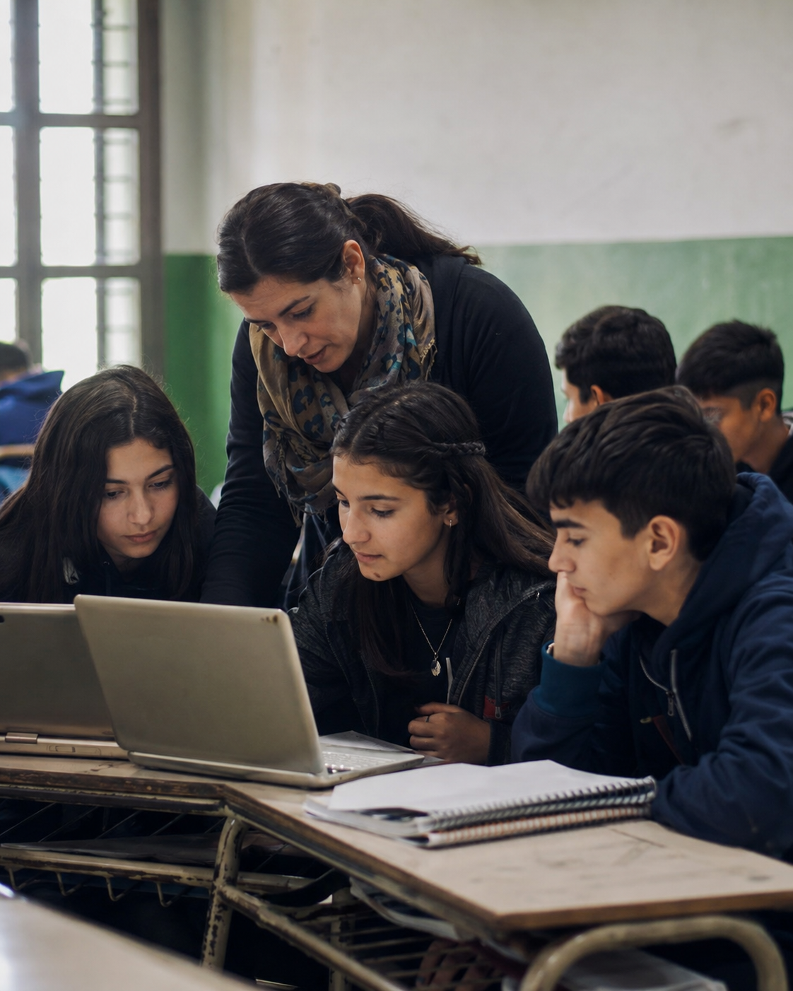 Docente y estudiantes trabajando con dispositivos digitales en el aula